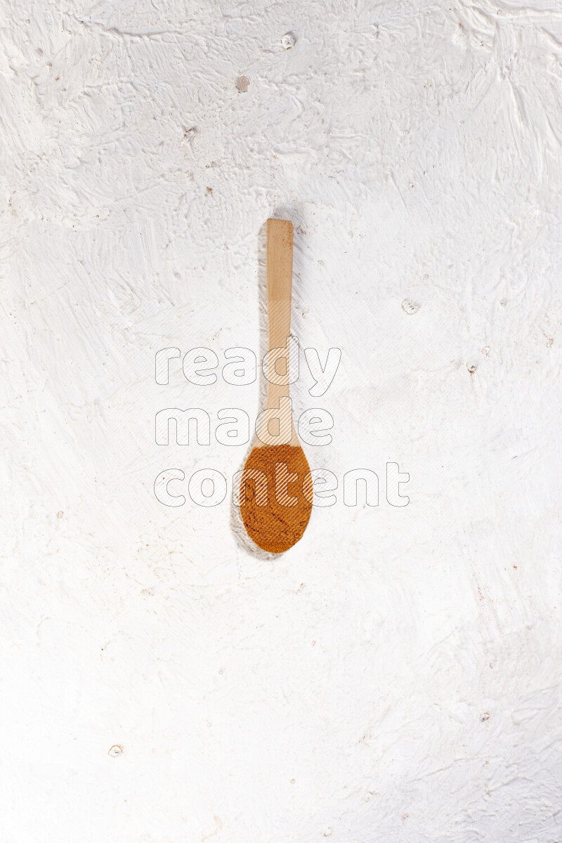 A wooden spoon full of ground paprika powder on white background