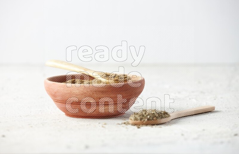 A wooden bowl and 2 wooden spoons full of cumin powder and cumin seeds on textured white flooring