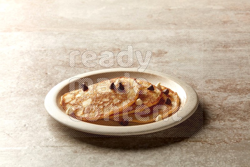 Three stacked chocolate chips pancakes in a beige plate on beige background