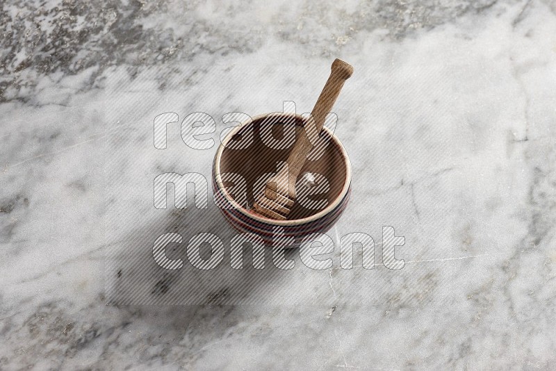 Multicolored Pottery bowl with wooden honey handle in it, on grey marble flooring, 65 degree angle