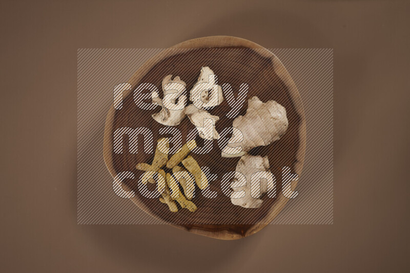 An assorted whole spices on a flat wooden tray including fresh and dried ginger, cinnamon sticks, cardamom, turmeric fingers, cloves, star anise on beige background