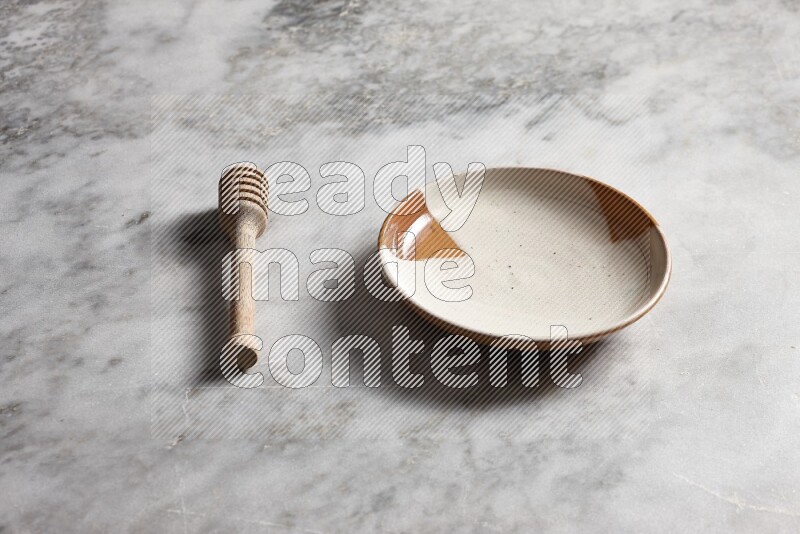 Multicolored pottery plate with wooden honey dipper on the side on grey marble background