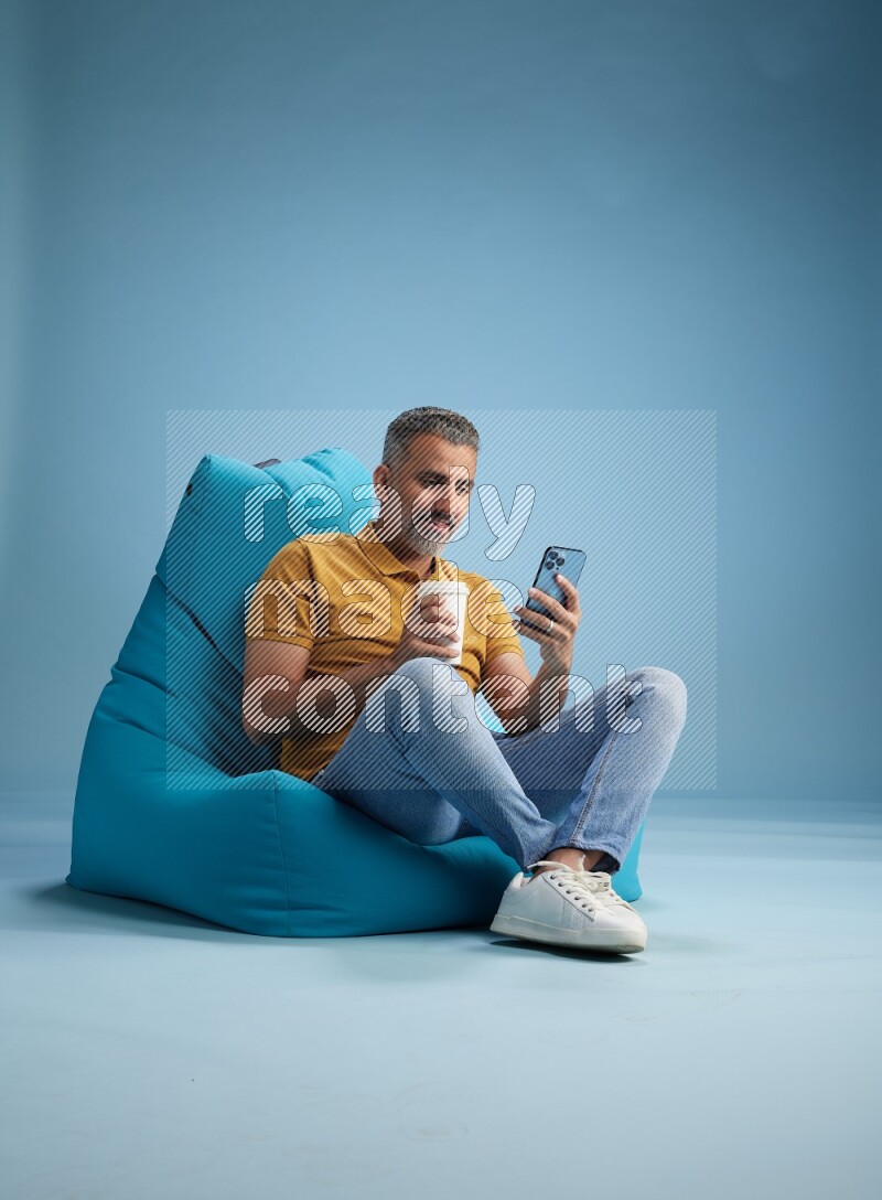 A man sitting on a blue beanbag and drinking coffee