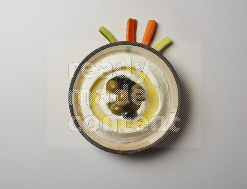 Lebnah garnished with whole black olives in a pottery plate on a white background
