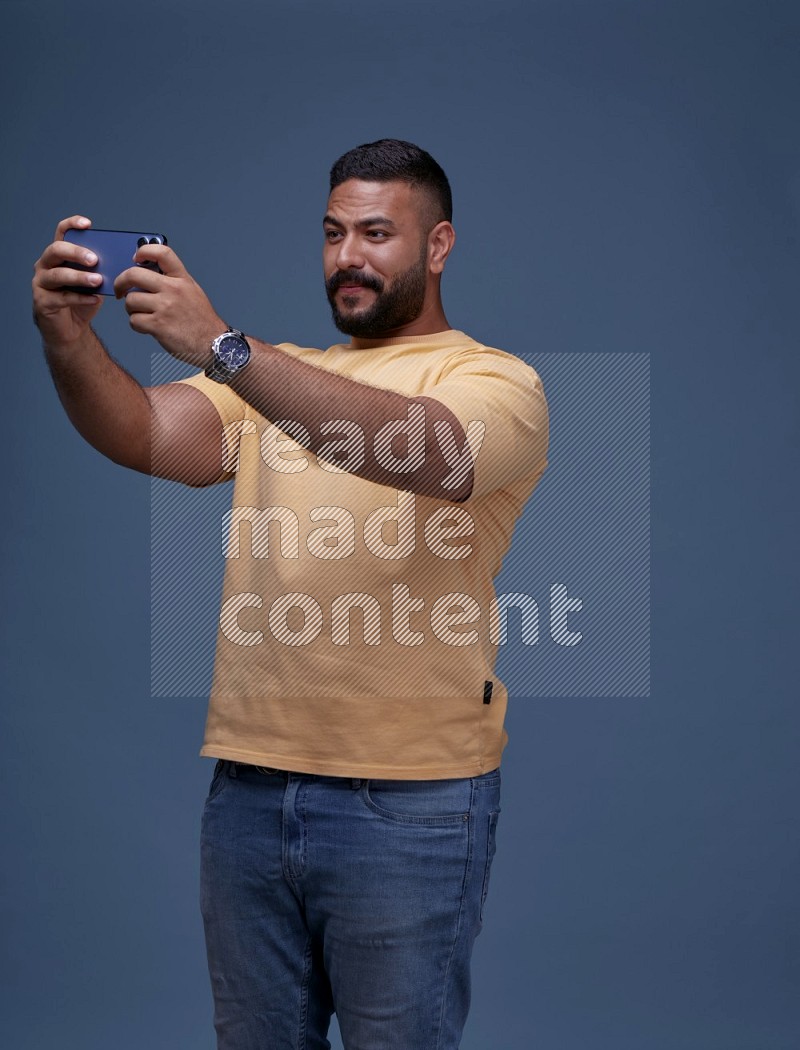 A man Playing Games on Smartphone on Blue Background wearing Orange T-shirt