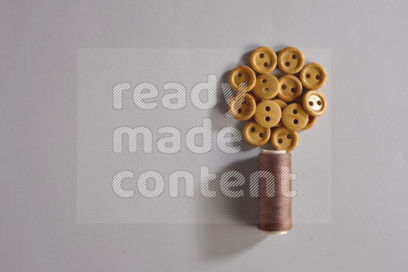 A brown sewing thread spool with colored buttons on grey background