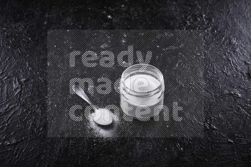 A glass jar full of fine table salt on black background