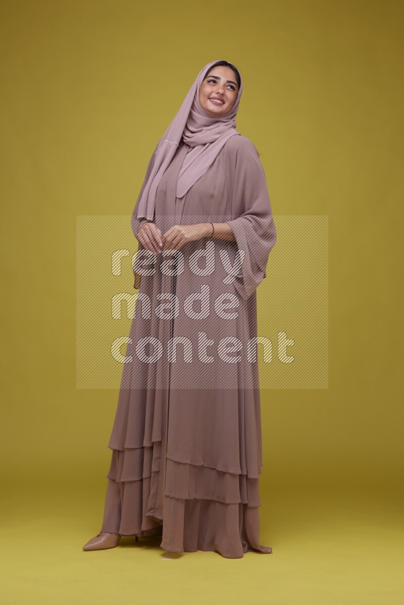 A woman Posing on a Yellow Background wearing Brown Abaya with Hijab