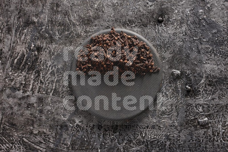 Cloves on a black plate on textured black background