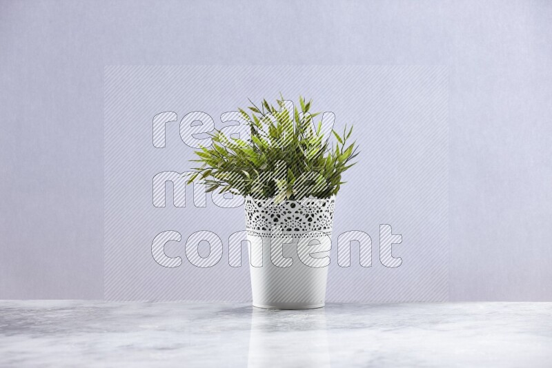 Green artificial plant in white decorative pot on grey marble background