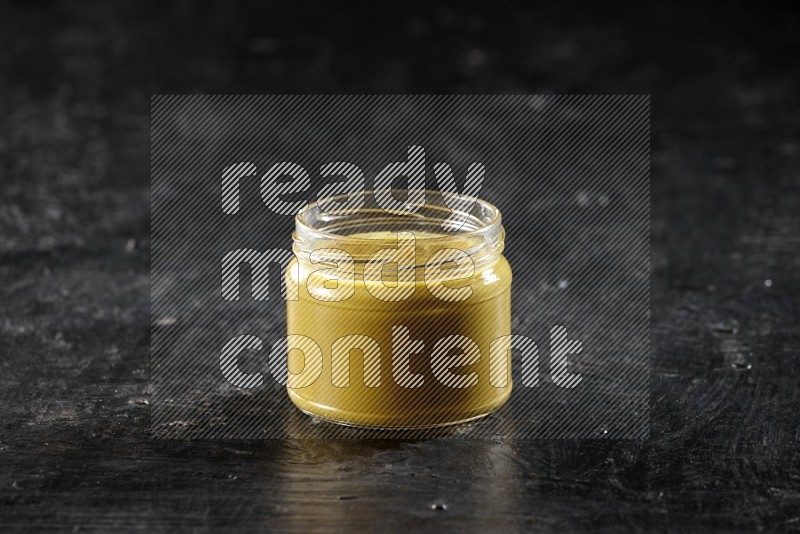 A glass jar full of mustard paste on a textured black flooring in different angles