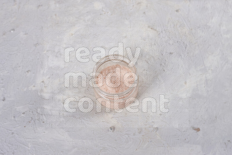 A glass jar full of fine himalayan salt on white background