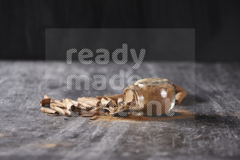 Herbal glass jar full cinnamon powder flipped and a metal spoon full of powder surrounded by cinnamon sticks on textured black background in different angles
