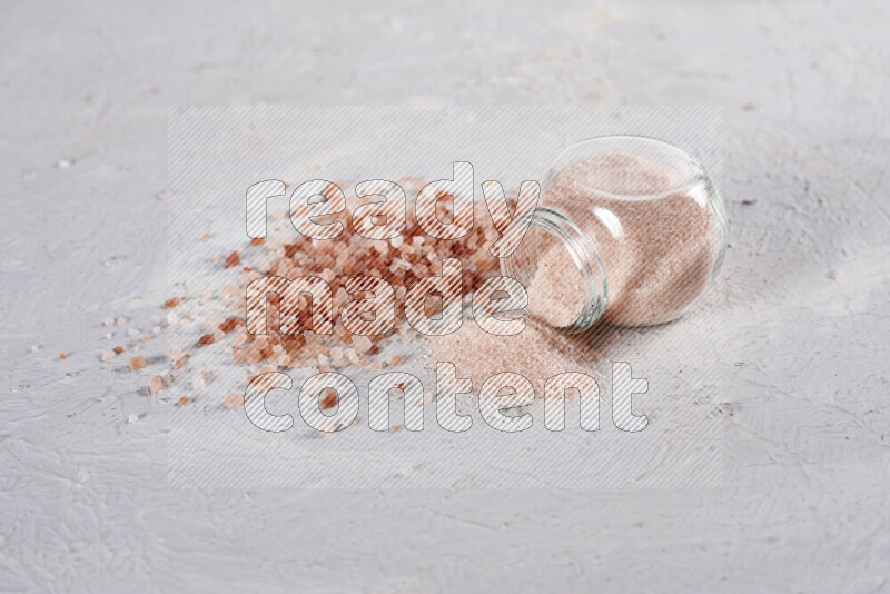 A glass jar full of fine himalayan salt with some himalayan crystals beside it on a white background