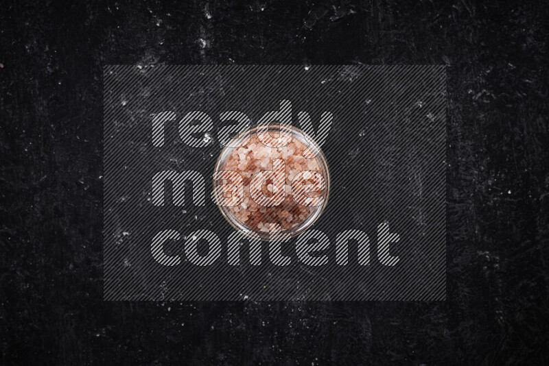 A glass jar full of coarse himalayan salt crystals on black background