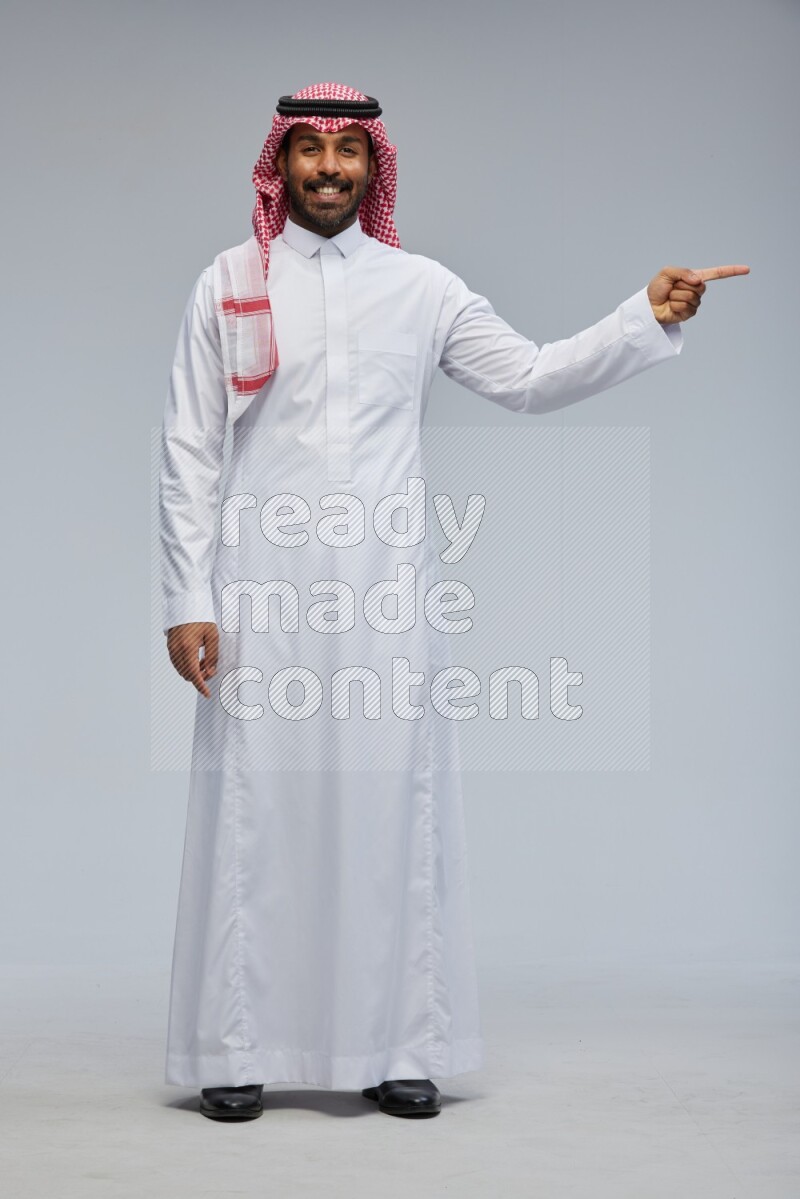 Saudi man Wearing Thob and shomag standing interacting with the camera on Gray background