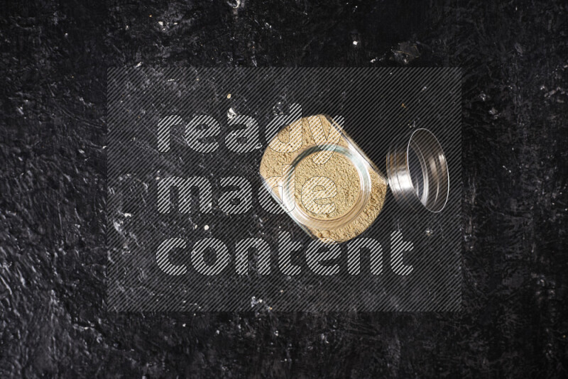 A glass jar full of ground ginger powder on black background