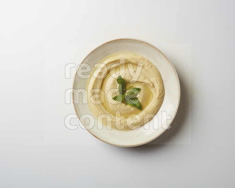 Hummus in a pottry plate garnished with mint  on a white background