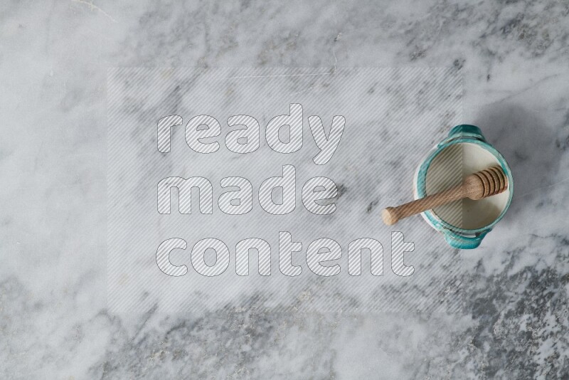 Multicolored pottery bowl with wooden honey dipper in it on grey marble background