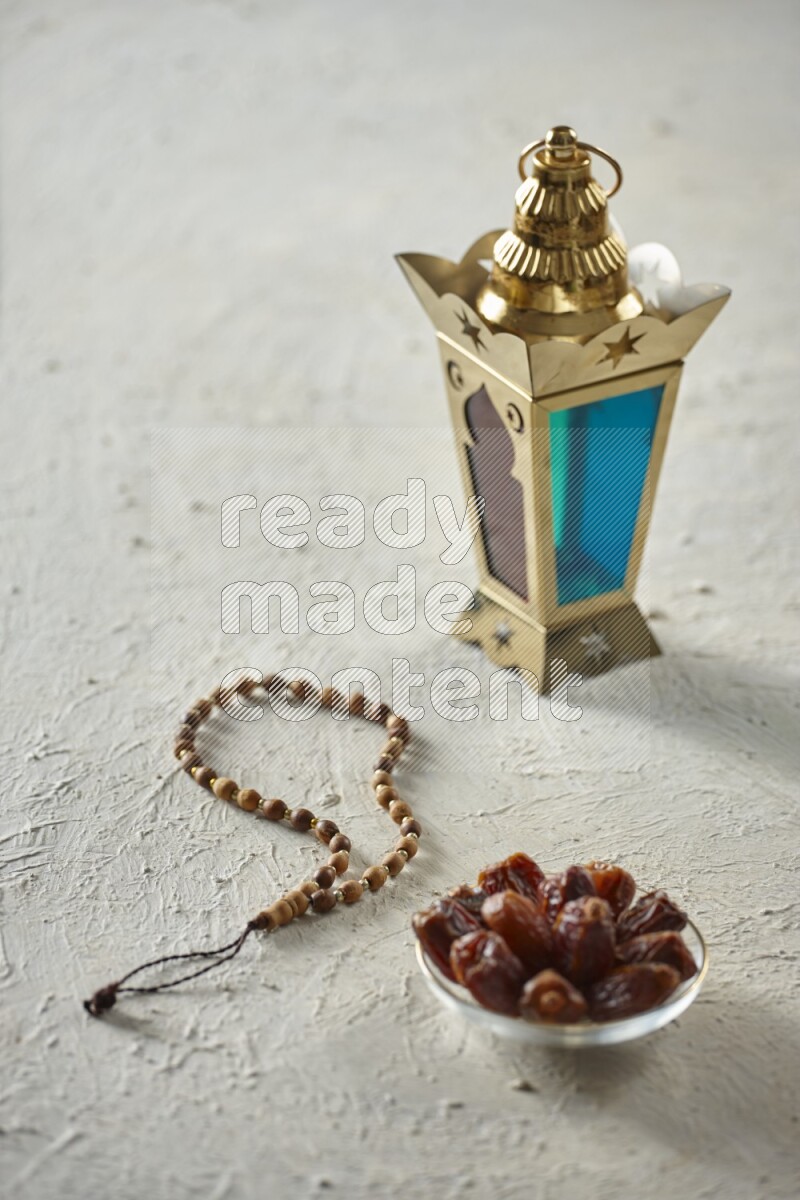 A golden lantern with different drinks, dates, nuts, prayer beads and quran on textured white background