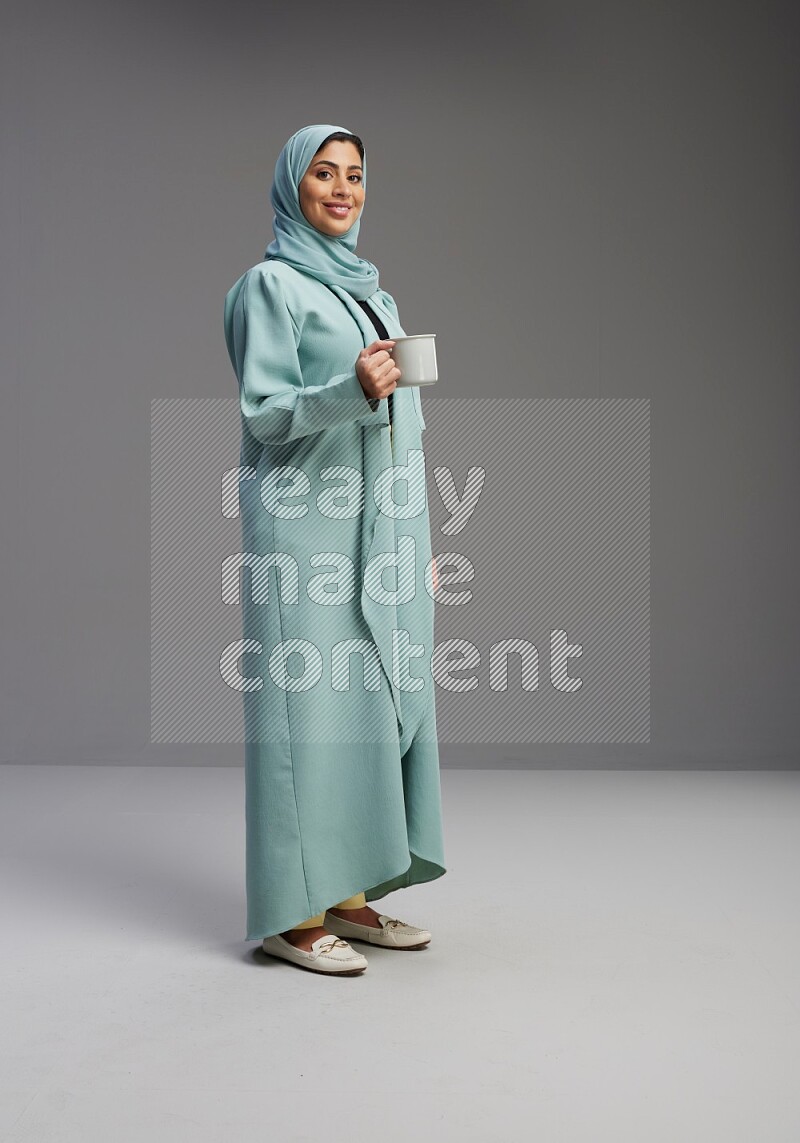 Saudi Woman wearing Abaya standing  holding a mug on Gray background