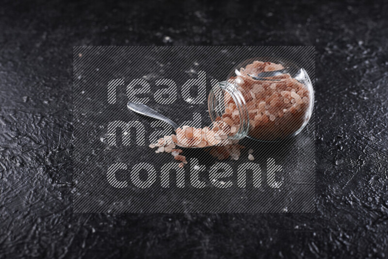 A glass jar full of coarse himalayan salt crystals on black background