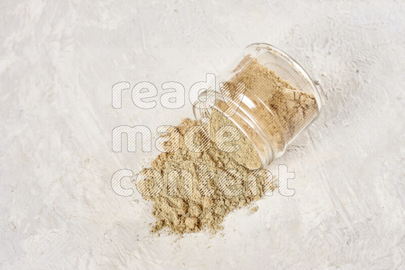 A glass jar full of ground ginger powder flipped with some spilling powder on white background