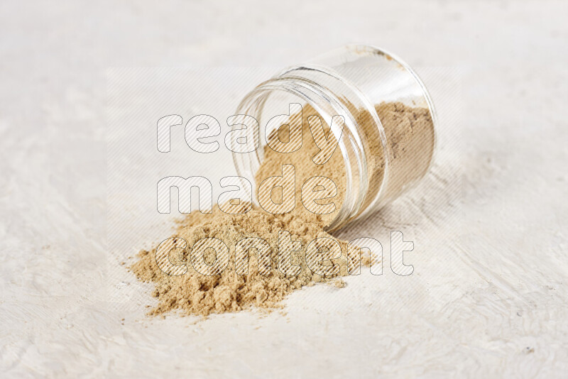 A glass jar full of ground ginger powder flipped with some spilling powder on white background