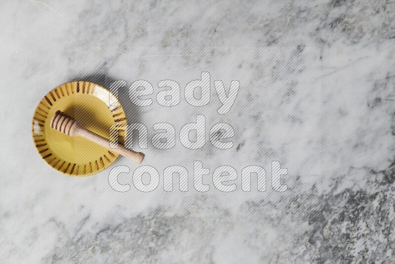 Multicolored pottery plate with wooden honey dipper in it on grey marble background