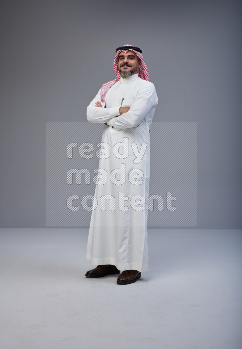 Saudi man Wearing Thob and red Shomag standing with crossed arms on Gray background