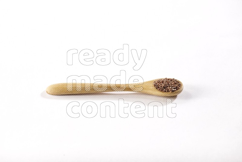 A wooden spoon full of flax seeds on a white flooring