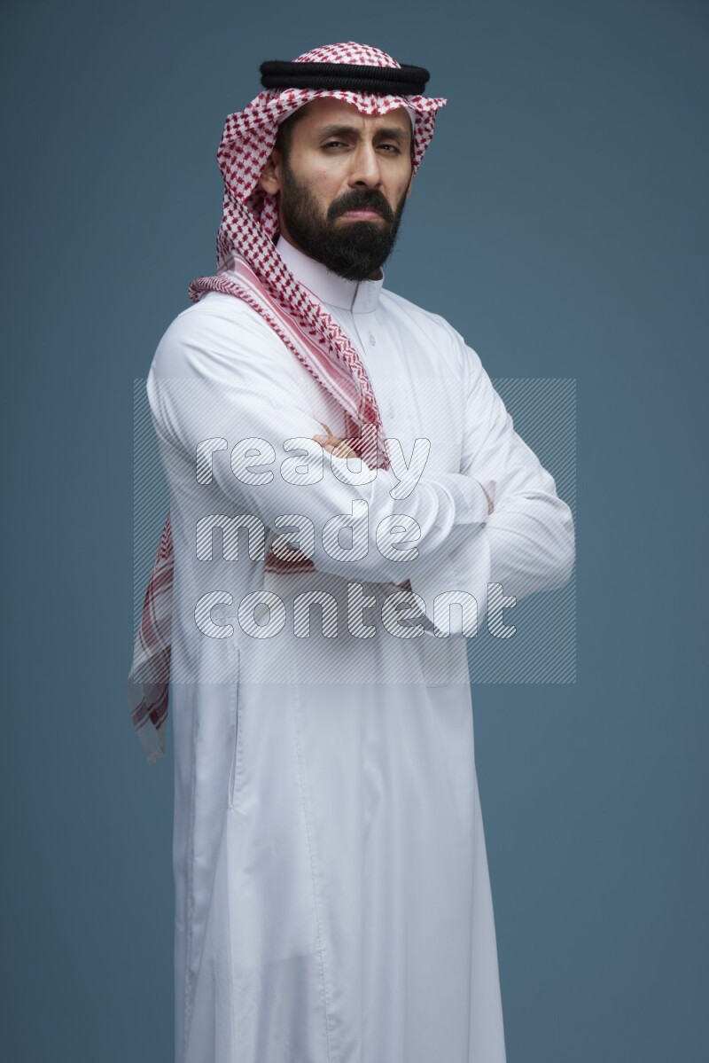 A man posing in a blue background wearing Saudi Thob and Shomag