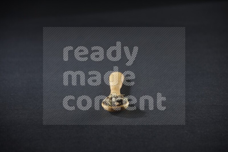 A wooden spoon full of cardamom on black flooring