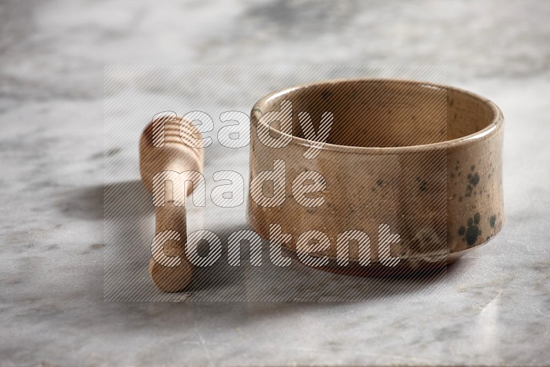 Beige Pottery bowl with wooden honey handle on the side with grey marble flooring, 15 degree angle