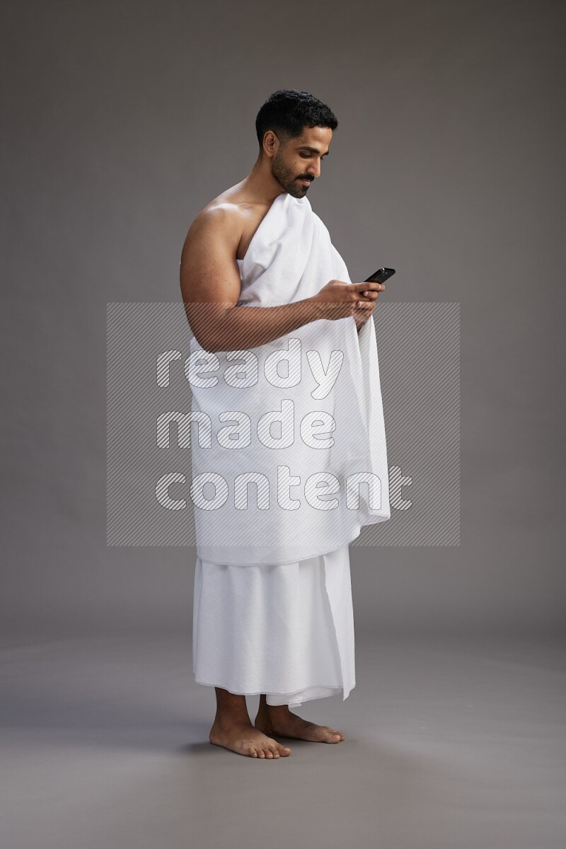 A man wearing Ehram Standing texting on phone on gray background