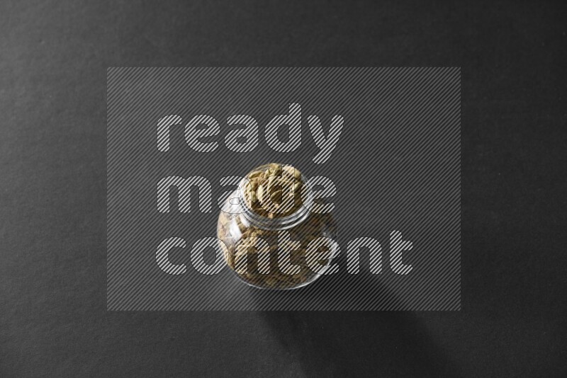 A glass spice jar full of cardamom on black flooring