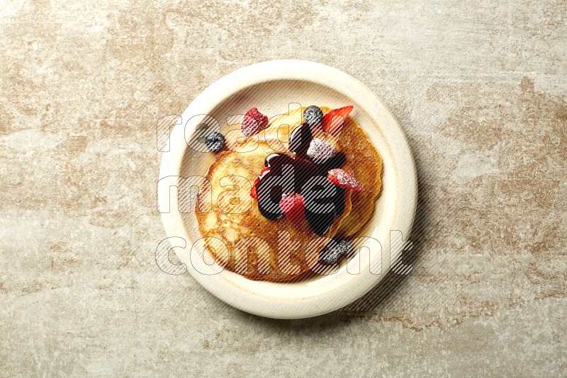 Three stacked mixed berries pancakes in a grey plate on beige background