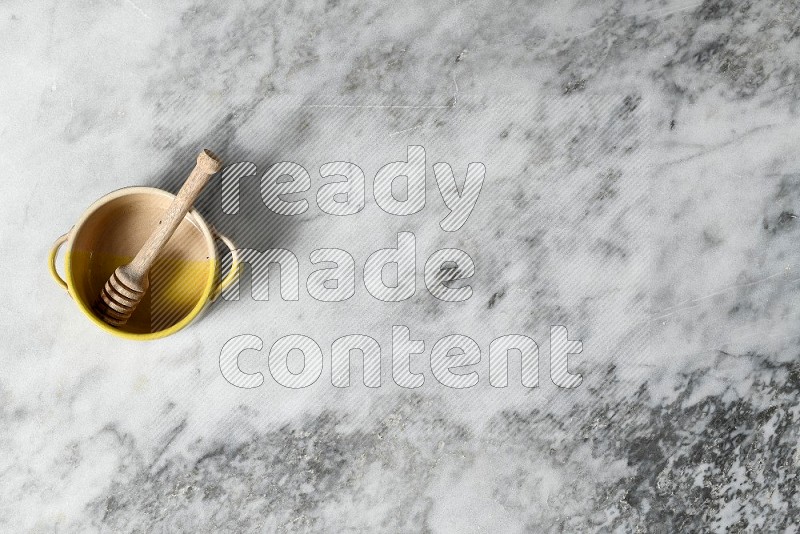 Multicolored Pottery Bowl with wooden honey handle in it, on grey marble flooring, Top View