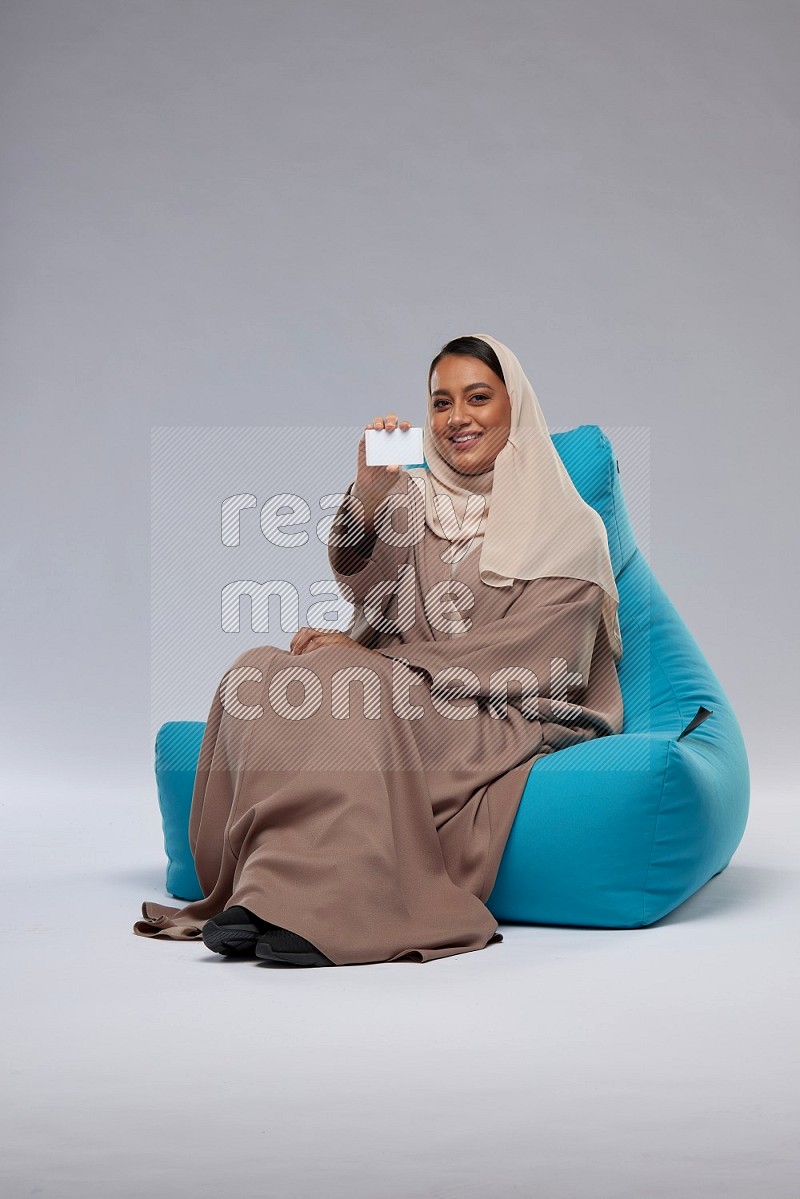 A Saudi woman sitting on a blue beanbag and holding ATM card