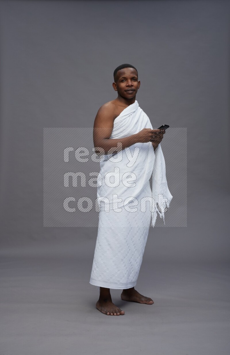 A man wearing Ehram Standing texting on phone on gray background