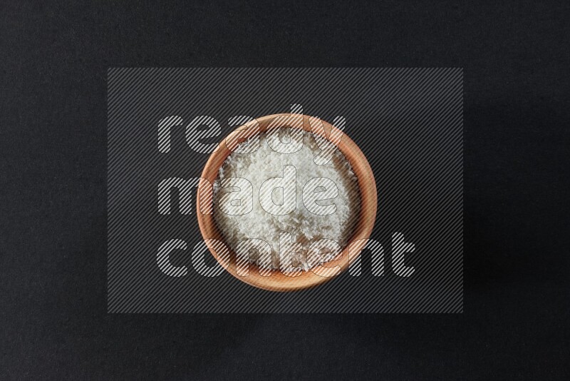 A wooden bowl full of desiccated coconut on a black background in different angles