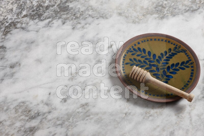 Decorative pottery plate with wooden honey dipper in it on grey marble background