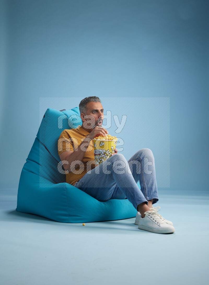 A man sitting on a blue beanbag and eating popcorn