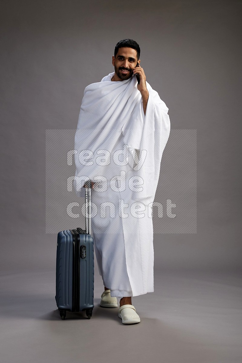 A man wearing Ehram Standing holding traveling bag on gray background