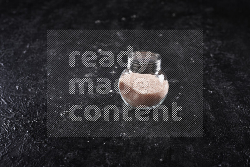 A glass jar full of fine himalayan salt on black background