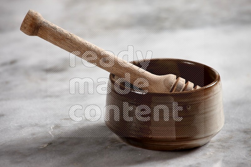 Brown Pottery bowl with wooden honey handle in it, on grey marble flooring, 15 degree angle