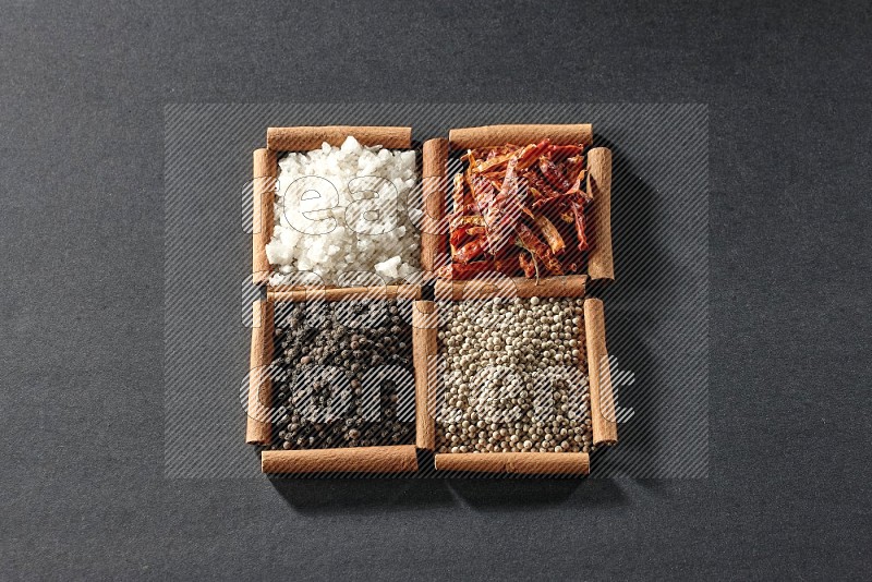 4 squares of cinnamon sticks full of black pepper, white pepper, dried red chilis and white salt on black flooring