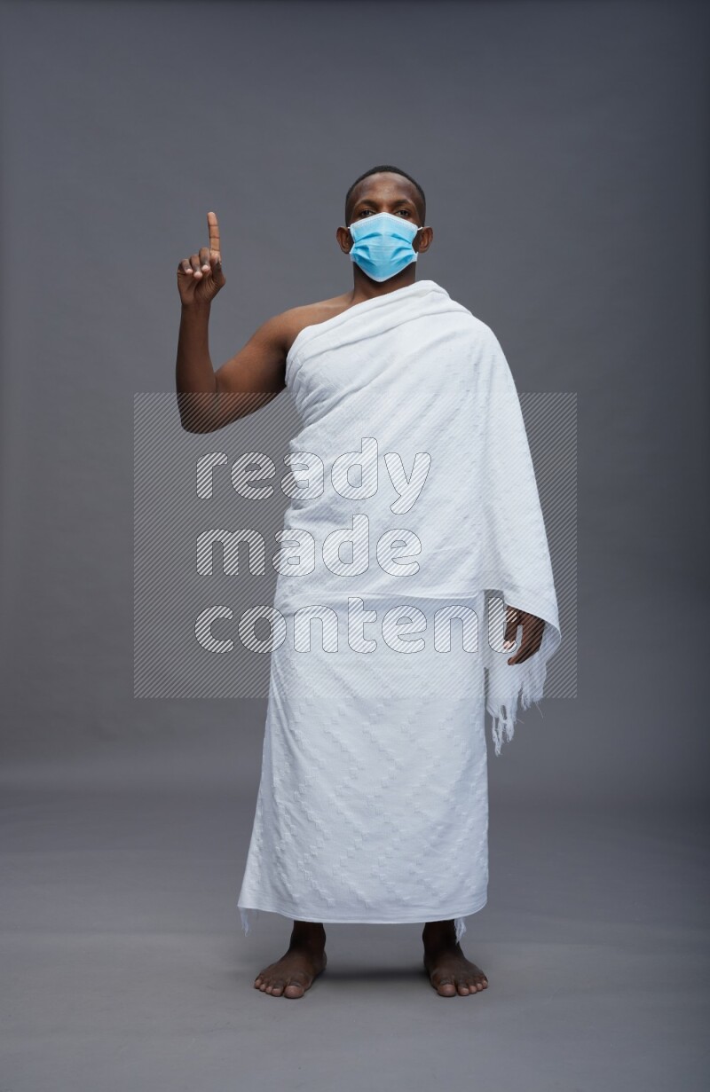 A man wearing Ehram with face mask Standing Interacting with the camera on gray background