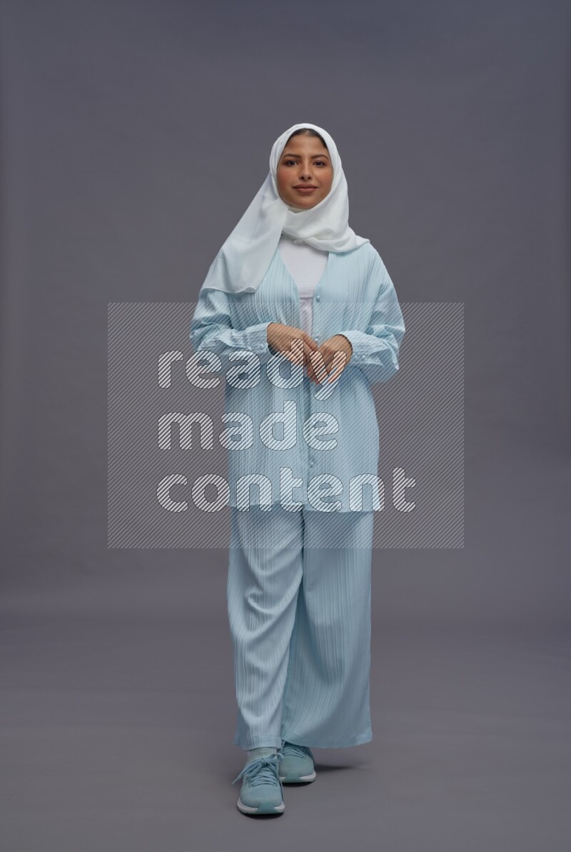 Saudi woman wearing hijab clothes standing interacting with the camera on gray background