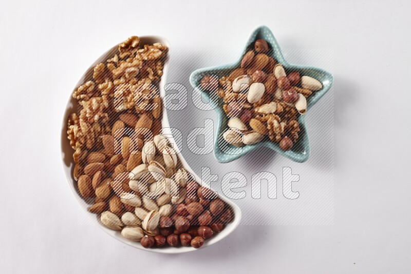 Mixed nuts in a crescent pottery plate and a star shaped plate on white background